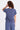 a woman facing backwards wearing a short sleeve blue twill shirt with a seam down the center and matching blue pants on a white background 