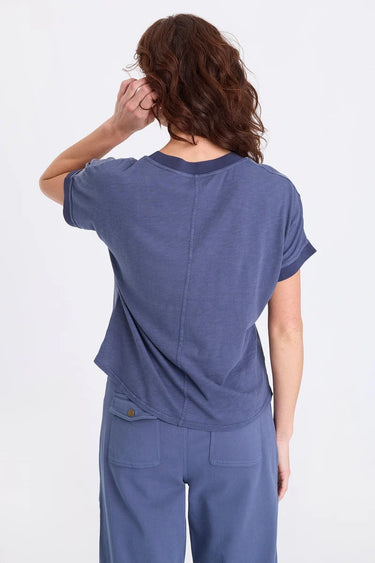 a woman facing backwards wearing a short sleeve blue twill shirt with a seam down the center and matching blue pants on a white background 