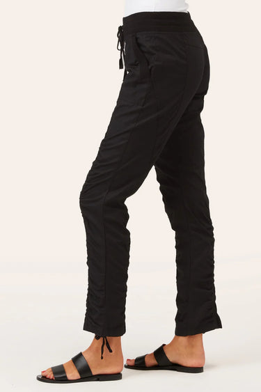 Black ruched ankle-length pants with a drawstring waist, shown on a model from the side against a light beige background.