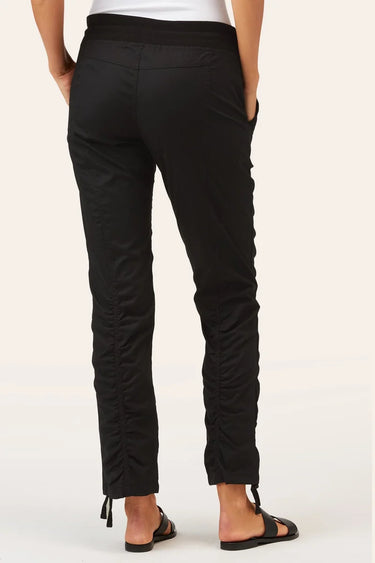 Black ruched ankle-length pants shown from the back on a model, paired with a white top and black sandals, against a light beige studio background.