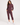 A woman modeling a matching burgundy zip-up jacket and cropped jogger pants set, paired with white sneakers, against a plain light gray studio background.