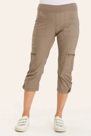 A person wearing taupe-brown cropped cargo pants with side flap pockets and gathered cuffs, paired with white sneakers, shown against a plain light beige studio background.