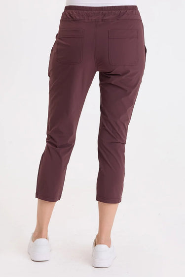 A back angle of a woman wearing leggings with a drawstring waist with zippered mini pockets team up with ruched front leg panels, front/back pockets and a cropped silhouette.