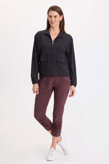 A woman wearing a black active jacket and berry pants on a whit background