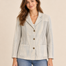 A woman modeling a light beige linen-blend blazer with brown buttons, worn over a white top and blue jeans, against a solid beige background.