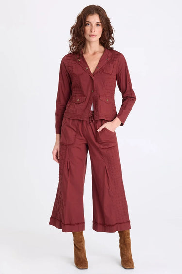 A woman wearing a blazer sports grid pintucking, rib contrast panels and brass hardware and matching berry pants on a white background.