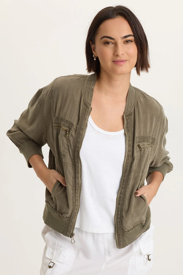 A woman wearing a white tank and a moss green cargo jacket with white pants