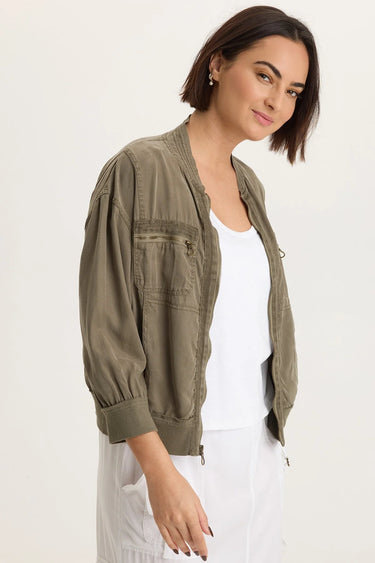 a woman wearing a white tank and pants with a moss green jacket