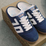 A pair of blue and white retro-style low-top sneakers resting on a brown patterned shoebox, placed on a gray concrete floor.