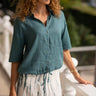 Woman wearing a teal shirt and white skirt with green stripes, standing outdoors.