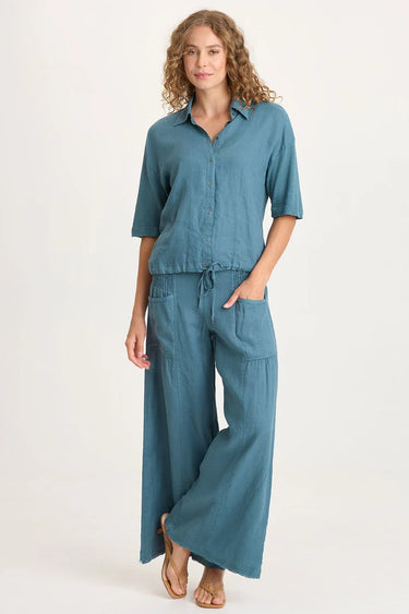 Woman wearing a teal outfit with a shirt and wide-leg pants on a white background