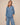 A woman modeling a matching light blue denim two-piece set, featuring a long-sleeve button-up shirt and wide-leg pants, against a solid beige studio background.