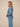 A woman in side profile wearing a light blue denim long-sleeve shirt and matching wide-leg pants against a solid beige studio background.
