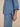 Close-up of a person wearing a light blue denim shirt and matching denim pants against a plain beige background.