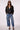A woman modeling a black cropped double-breasted jacket, blue wide-leg jeans, a white top, and black heels against a light gray studio background.