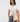 A woman wearing a white crewneck t-shirt and blue jeans, carrying a light beige leather crossbody bag with a silver-toned clasp over her shoulder, set against a white background.