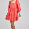 Woman wearing a coral dress with lace details on a plain background