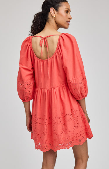 Woman wearing a coral dress with intricate cut-out details on a plain background