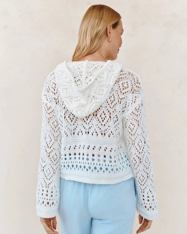 Woman wearing a white crochet hoodie against a beige background