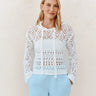 Woman wearing a white lace top and light blue pants against a plain background