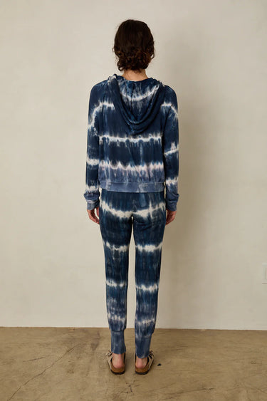 Person wearing a tie-dye hoodie and pants against a plain background
