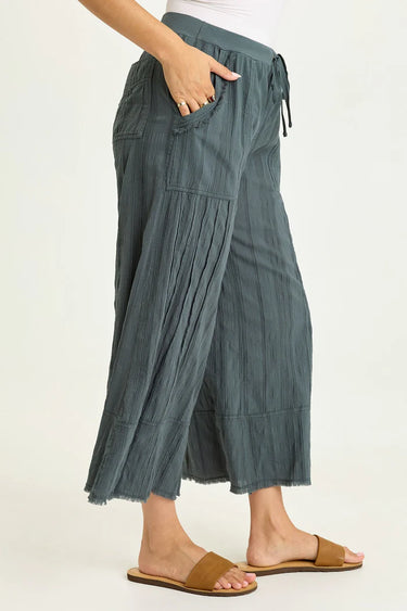 Person wearing teal pleated pants on a white background