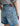 Person wearing blue denim shorts with a brand patch on a neutral background