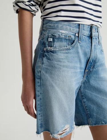 Person wearing a striped shirt and denim shorts on a plain background