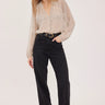 A woman wearing a black polka dot and cream blouse with black jeans on a white background.
