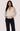 A woman wearing a black polka dot and cream blouse with black jeans on a white background.