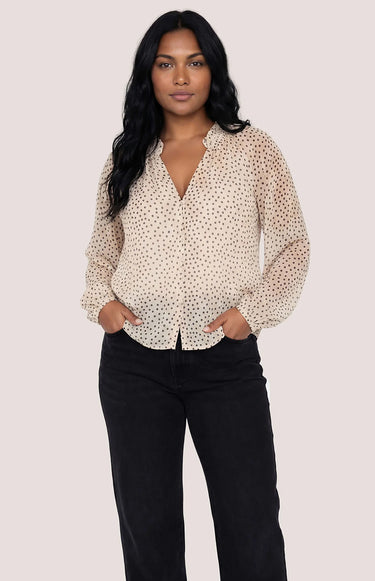 A woman wearing a black polka dot and cream blouse with black jeans on a white background.