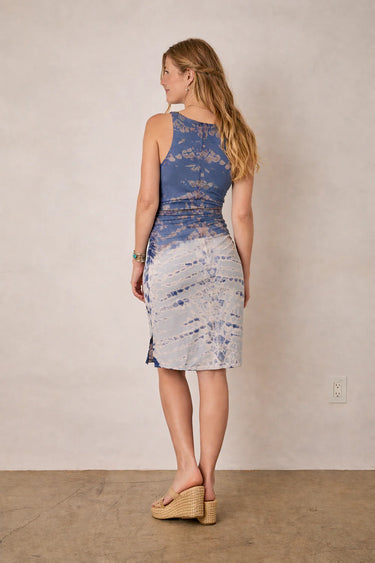 Woman wearing a tie-dye dress standing against a plain wall.