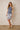 Woman wearing a tie-dye dress against a plain wall.