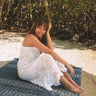 women wearing crochet white maxi skirt/dress sitting on a blanket on a sandy beach
