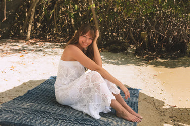 women wearing crochet white maxi skirt/dress sitting on a blanket on a sandy beach
