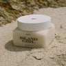 Jar of 'Island Girl' body scrub on sand with natural background