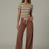 Woman wearing a striped crop top and brown wide-leg pants on a plain background