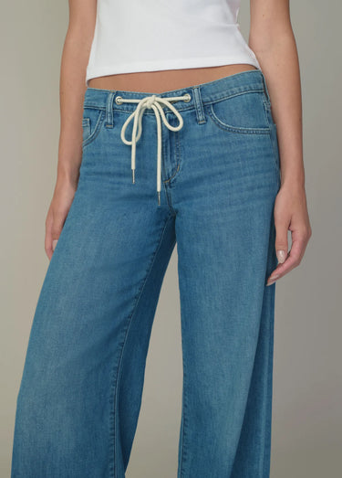 Person wearing blue jeans with a white top on a neutral background