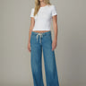 Woman wearing a white top and blue jeans against a neutral background