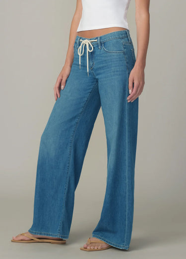 Person wearing blue jeans with a white top on a plain background