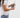 A woman in a white t-shirt and blue jeans holds a leopard print wallet with a tan leather strap and card slots against a white brick wall background.