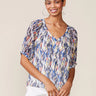 Woman wearing a colorful patterned blouse against a plain background