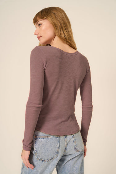 Woman wearing a long-sleeve brown top and jeans on a beige background