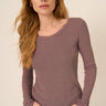 Woman wearing a long-sleeve mauve top against a beige background