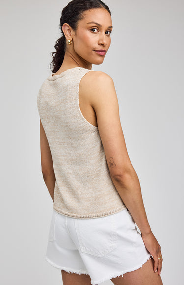 Woman wearing a beige sleeveless top and white shorts on a plain background