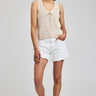 Woman wearing a beige sleeveless top and white shorts on a plain background