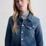 Woman wearing a blue denim jacket over a gray turtleneck on a light gray background