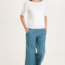 Woman wearing a white top and teal pants on a white background
