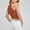 Woman wearing a brown tank top and white pants on a plain background