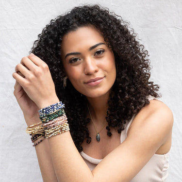Woman with curly hair wearing multiple bracelets on a light background